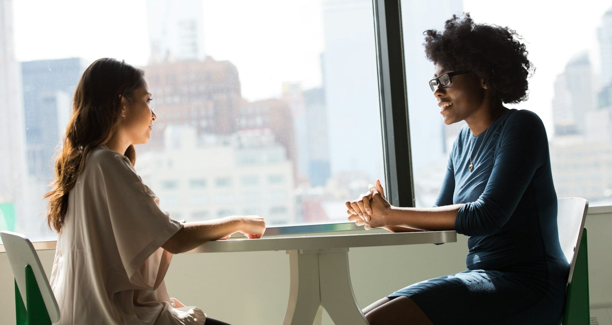 two women sitting beside table and talking